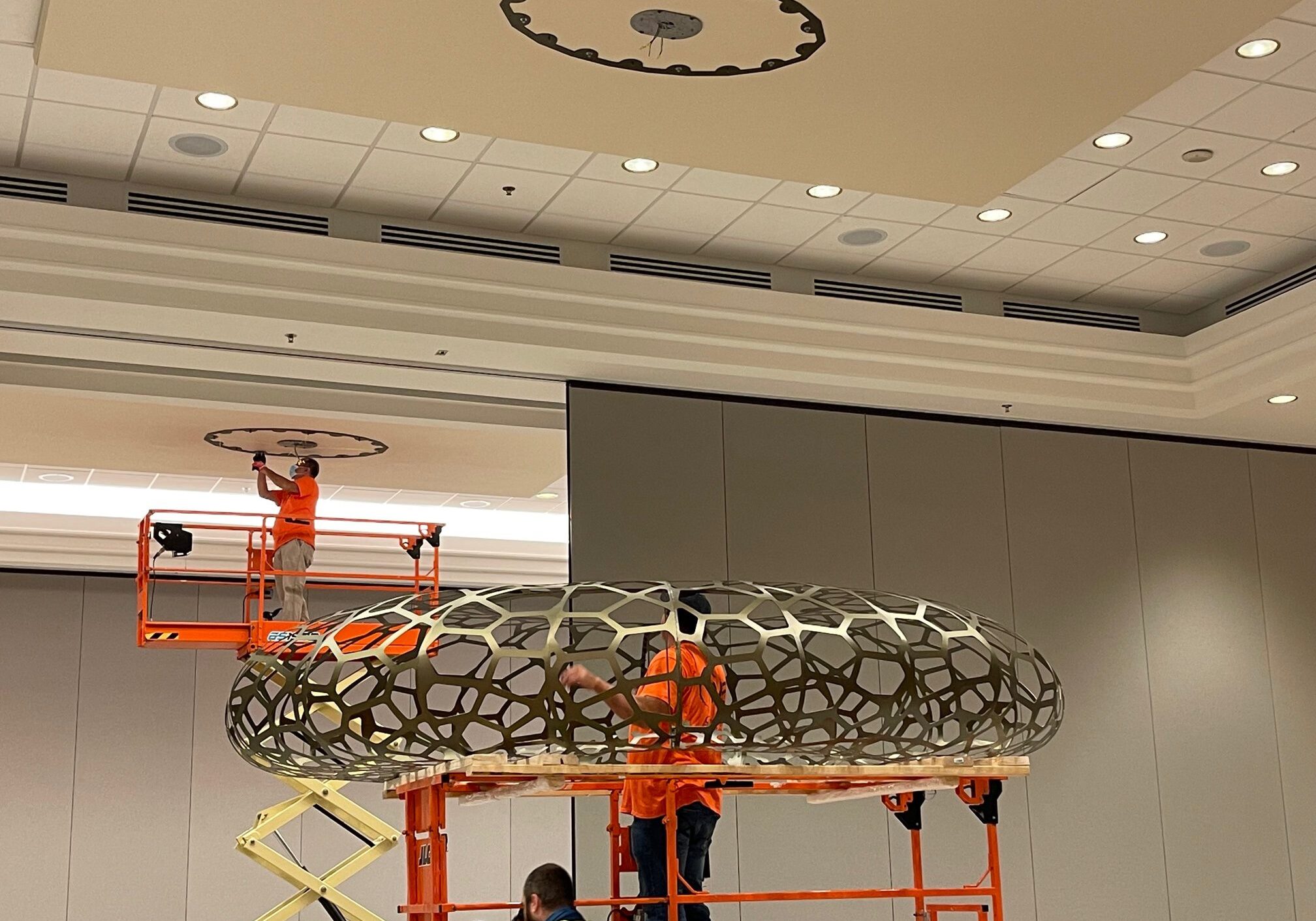 Workers installing large circular ceiling fixture.