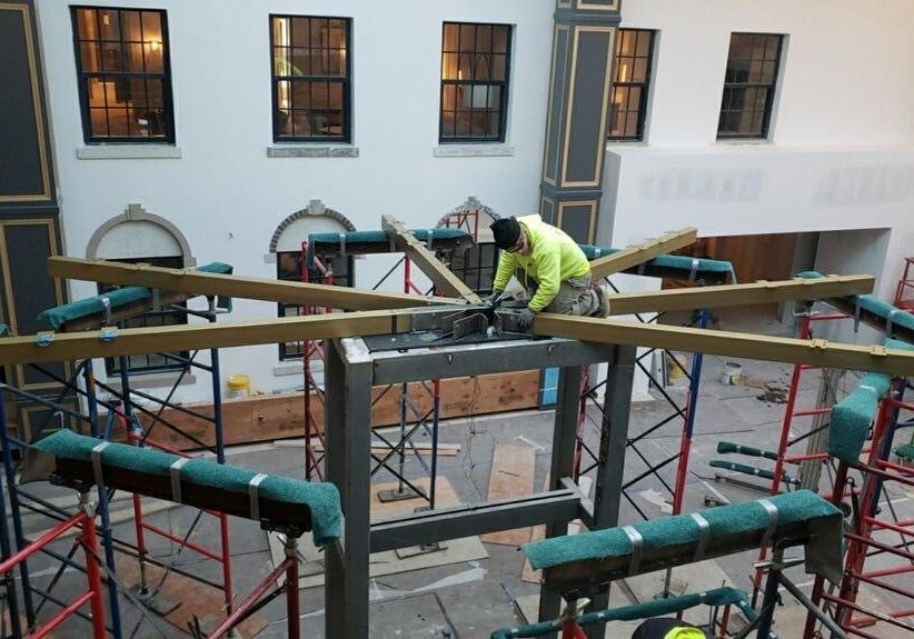 Worker assembling wooden beams on scaffolding.